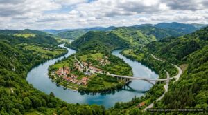 Vista aérea de rio cortando vale verde com cidade ribeirinha e ponte (imagem ilustrativa)